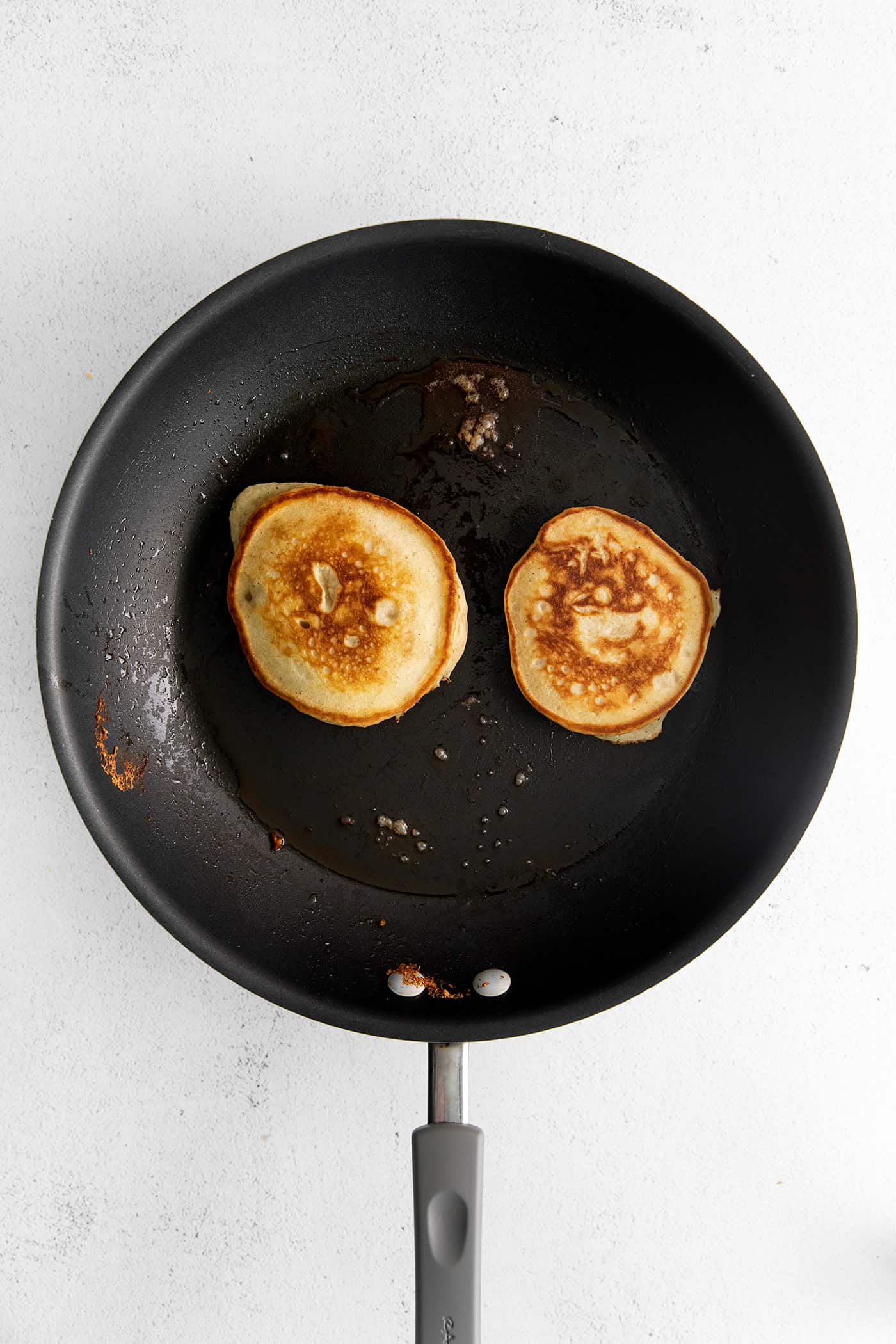 Made with pantry staples, these Buttermilk Pancakes are simply the best homemade pancakes you'll ever make! Super fluffy! Overhead view of two pancakes in a cast iron skillet