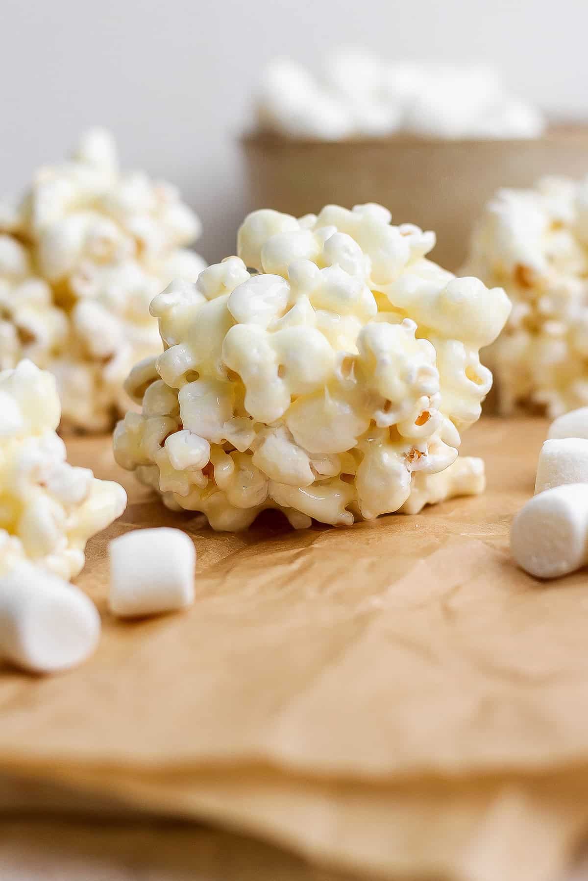 These easy Marshmallow Popcorn Balls are sweet and salty, crunchy and chewy, like a Rice Krispie treat made with popcorn instead of cereal! Marshmallow popcorn ball on parchment paper.