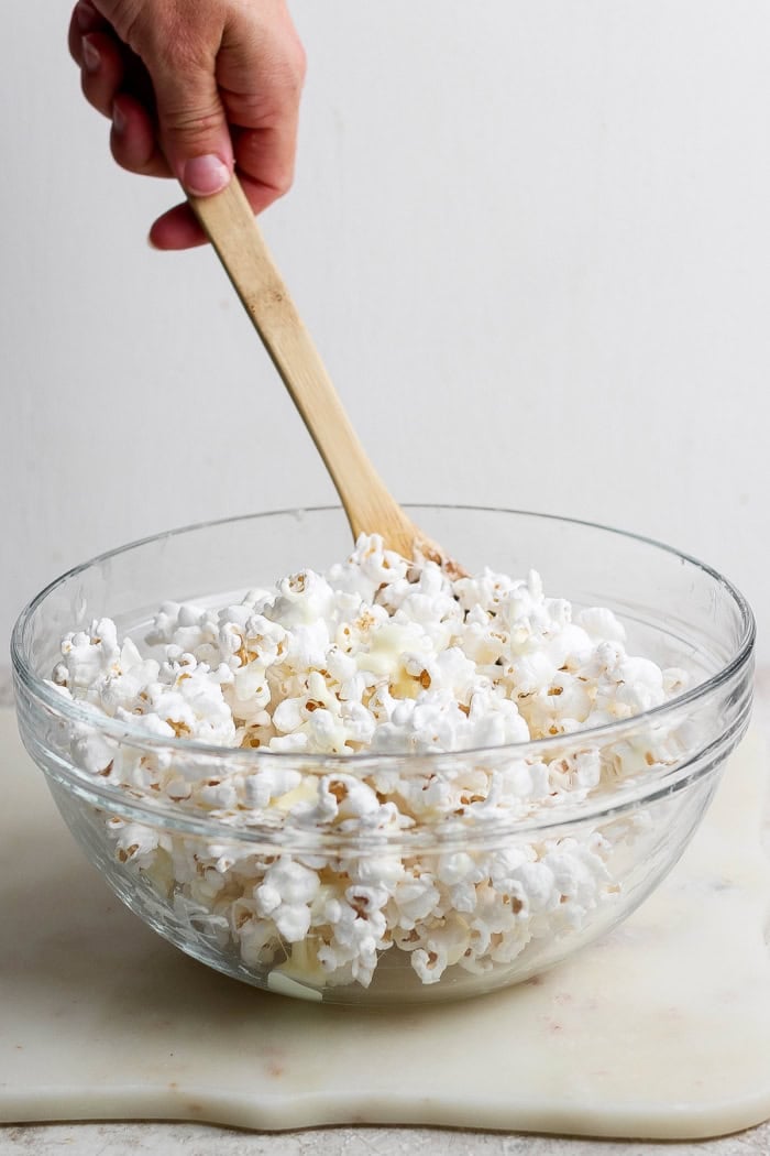 Stirring together popcorn and marshmallow mixture with wooden spoon.