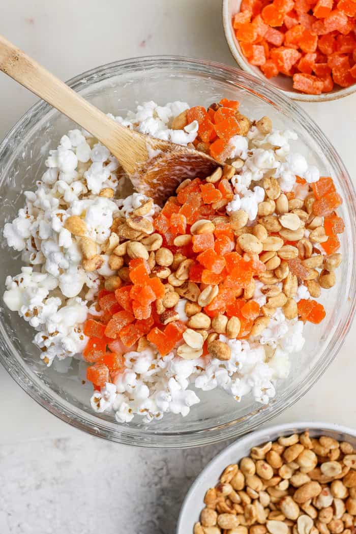 Orange gumdrops and peanuts added to bowl with marshmallow popcorn.