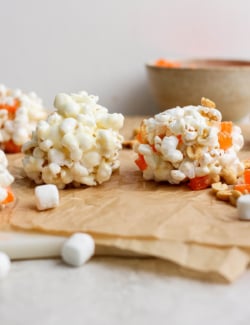 Two homemade marshmallow popcorn balls on parchment paper.