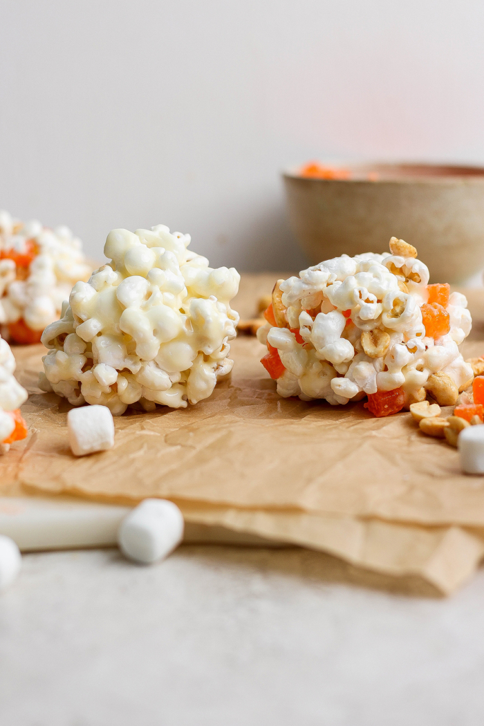 These easy Marshmallow Popcorn Balls are sweet and salty, crunchy and chewy, like a Rice Krispie treat made with popcorn instead of cereal! Two homemade marshmallow popcorn balls on parchment paper.