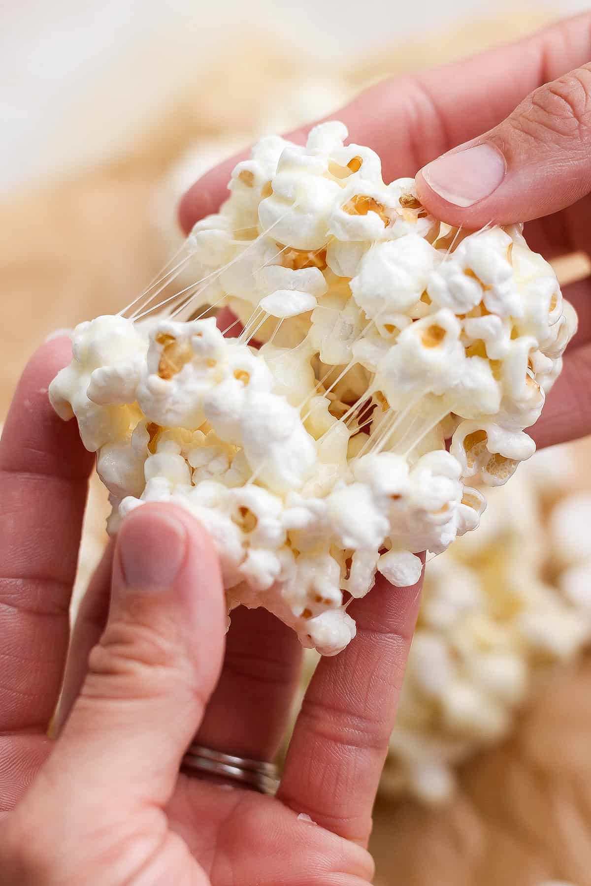 These easy Marshmallow Popcorn Balls are sweet and salty, crunchy and chewy, like a Rice Krispie treat made with popcorn instead of cereal! Hand pulling apart chewy marshmallow popcorn ball.