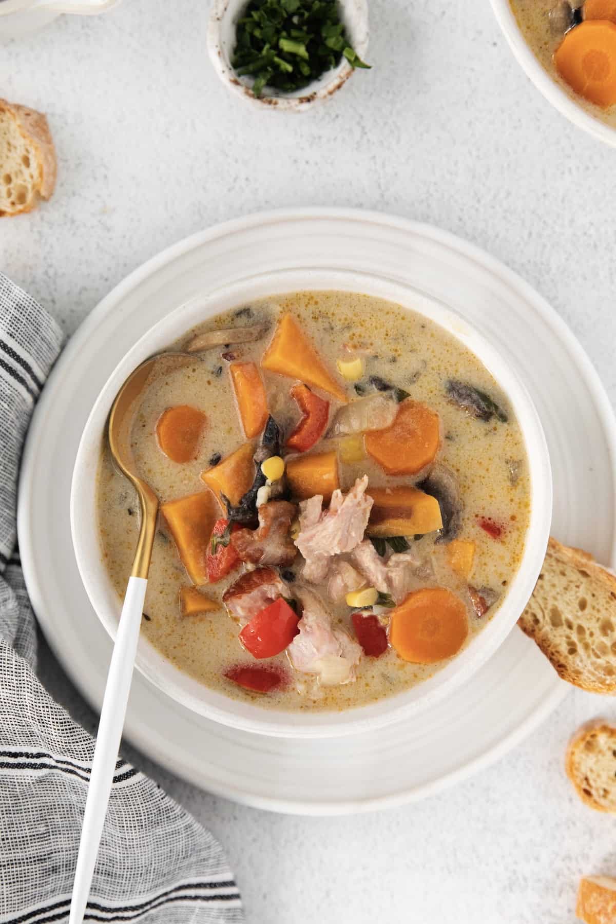 Make this easy Smoked Turkey Chowder recipe in one pot. It's lightly creamy and loaded with flavor, a great way to use up turkey leftovers! Overhead view of smoked turkey chowder in a white bowl with a spoon.