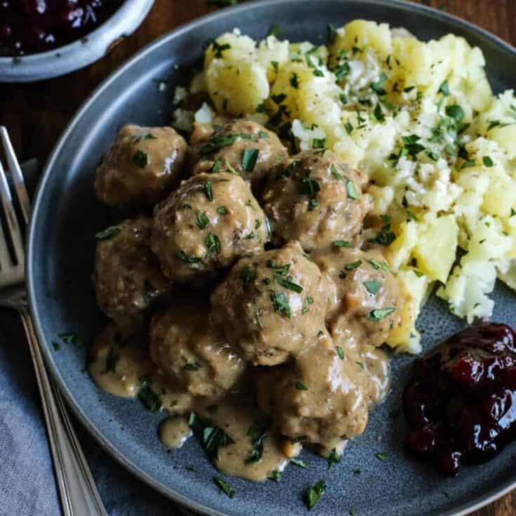 Swedish meatballs and gravy served with potatoes and lingonberry jam on a stoneware plate.