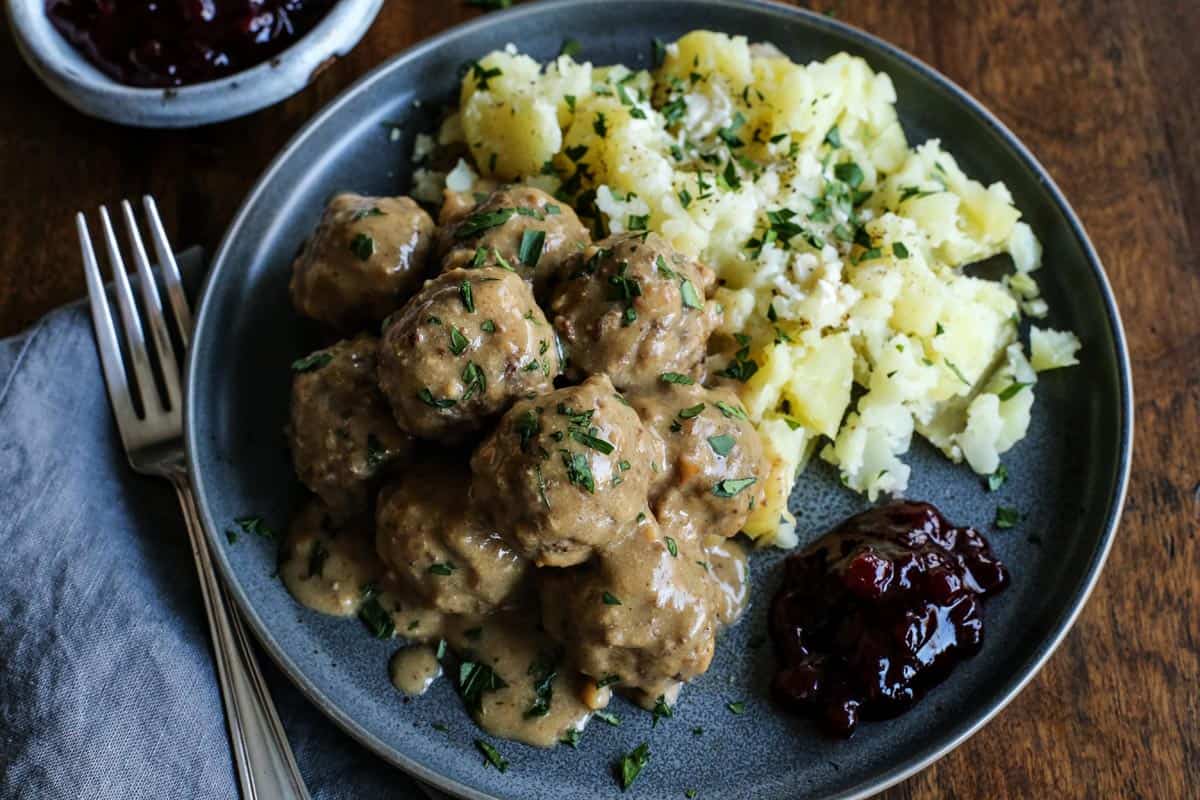 This easy Swedish meatballs recipe makes juicy, tender meatballs with a rich, creamy gravy. A homemade version of IKEA Swedish meatballs! Homemade IKEA Swedish meatballs and gravy served with potatoes and lingonberry jam on a stoneware plate.