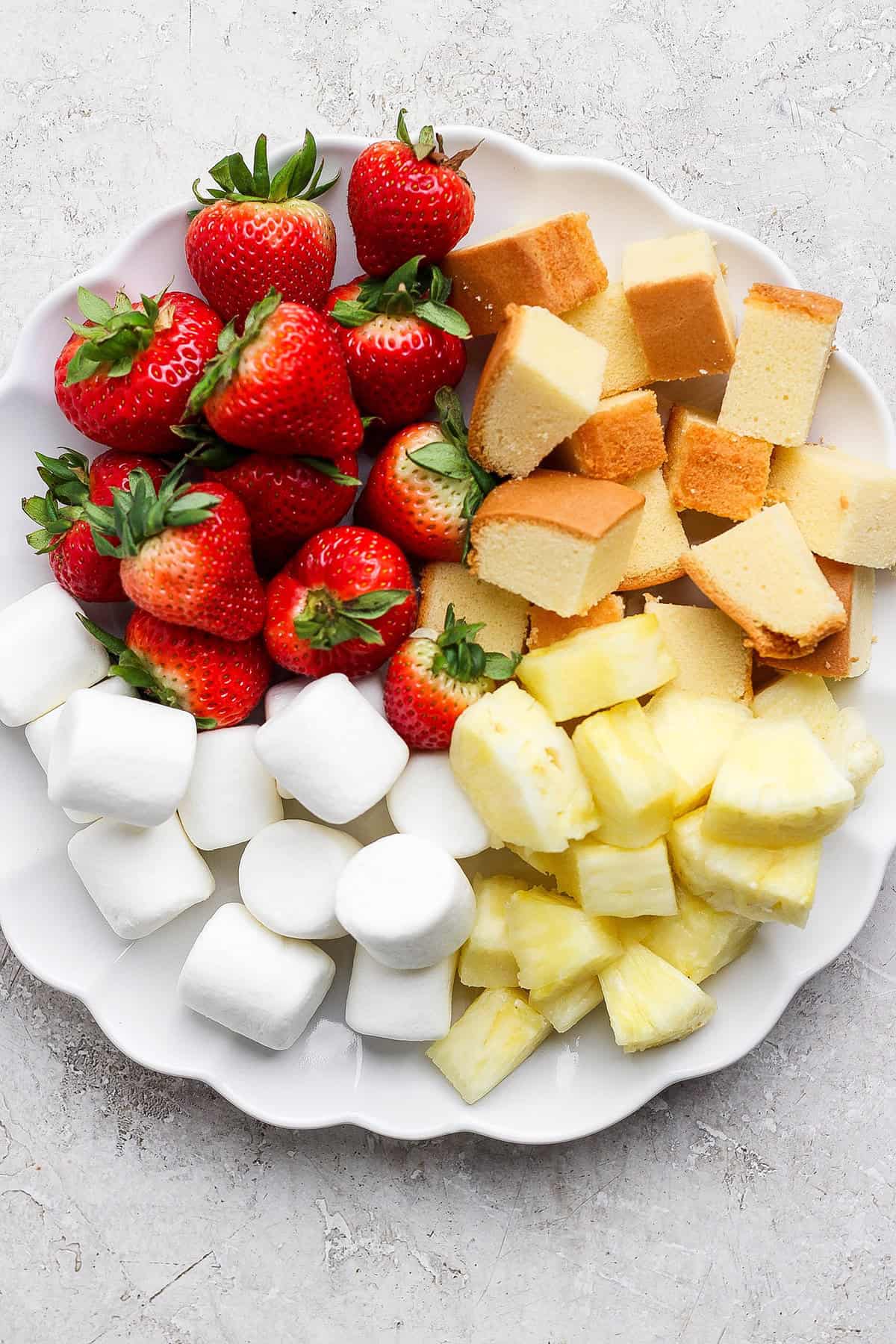 A secret ingredient makes this easy Chocolate Fondue the best ever! It’s rich, decadent and thick enough to stick to all your dippers. Marshmallows, strawberries, poundcake, and pineapple on plate