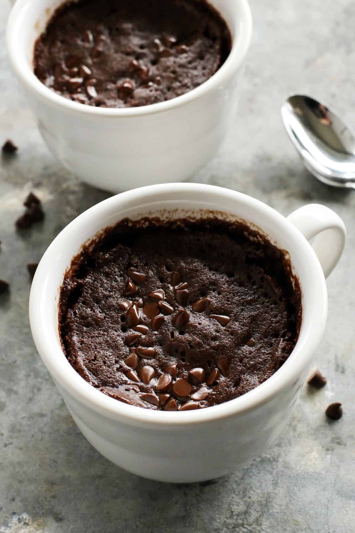 This gooey chocolate mug cake is fudgy, fluffy, and ready in minutes! Make this moist chocolate cake recipe with or without eggs. two white mugs of chocolate cake