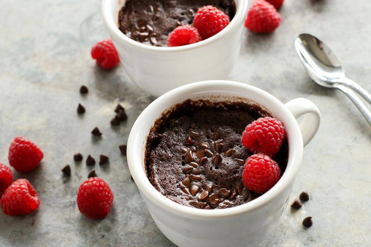 This gooey chocolate mug cake is fudgy, fluffy, and ready in minutes! Make this moist chocolate cake recipe with or without eggs. two mugs of chocolate cake and fresh raspberries