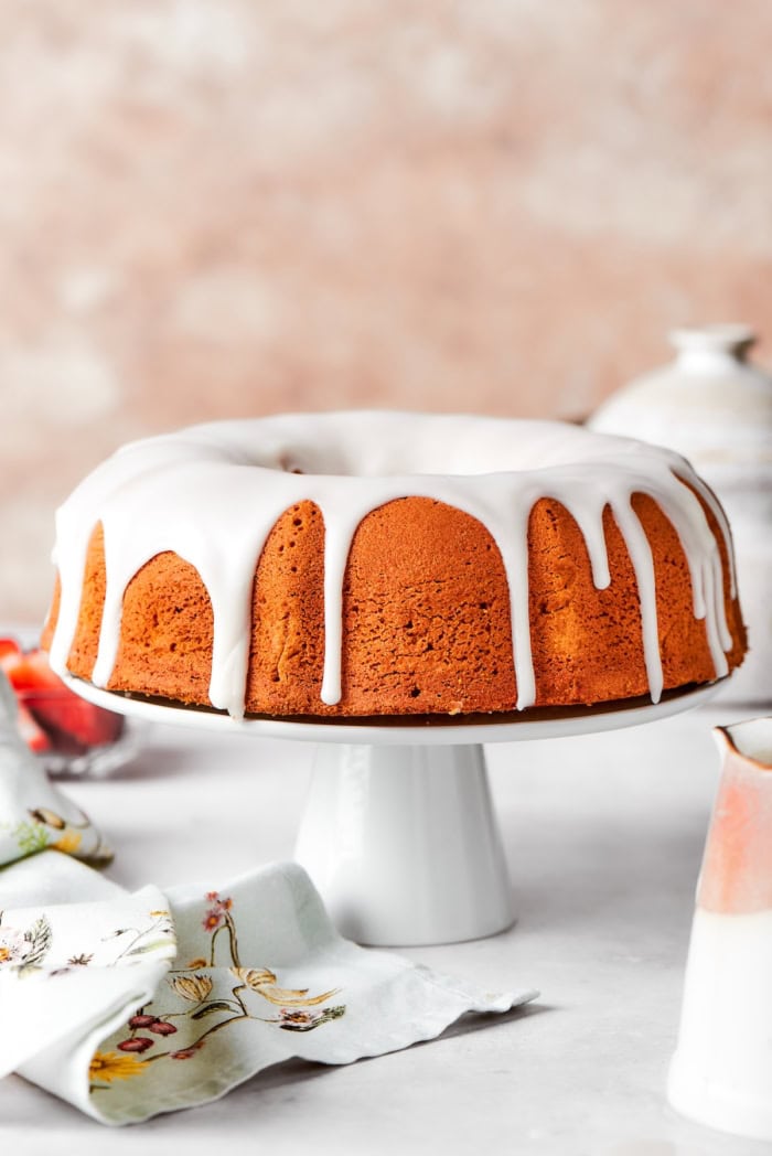 This cream cheese pound cake is a simple 6-ingredient recipe that’s rich, buttery, and perfectly dense with a velvety crumb. The best! Whole cream cheese pound cake on cake stand.