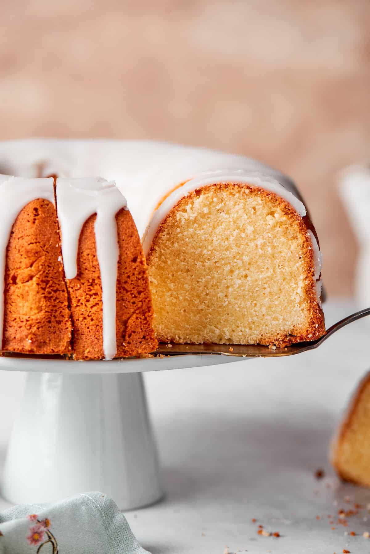 This cream cheese pound cake is a simple 6-ingredient recipe that’s rich, buttery, and perfectly dense with a velvety crumb. The best! Lifting slice of cream cheese pound cake from cake stand.