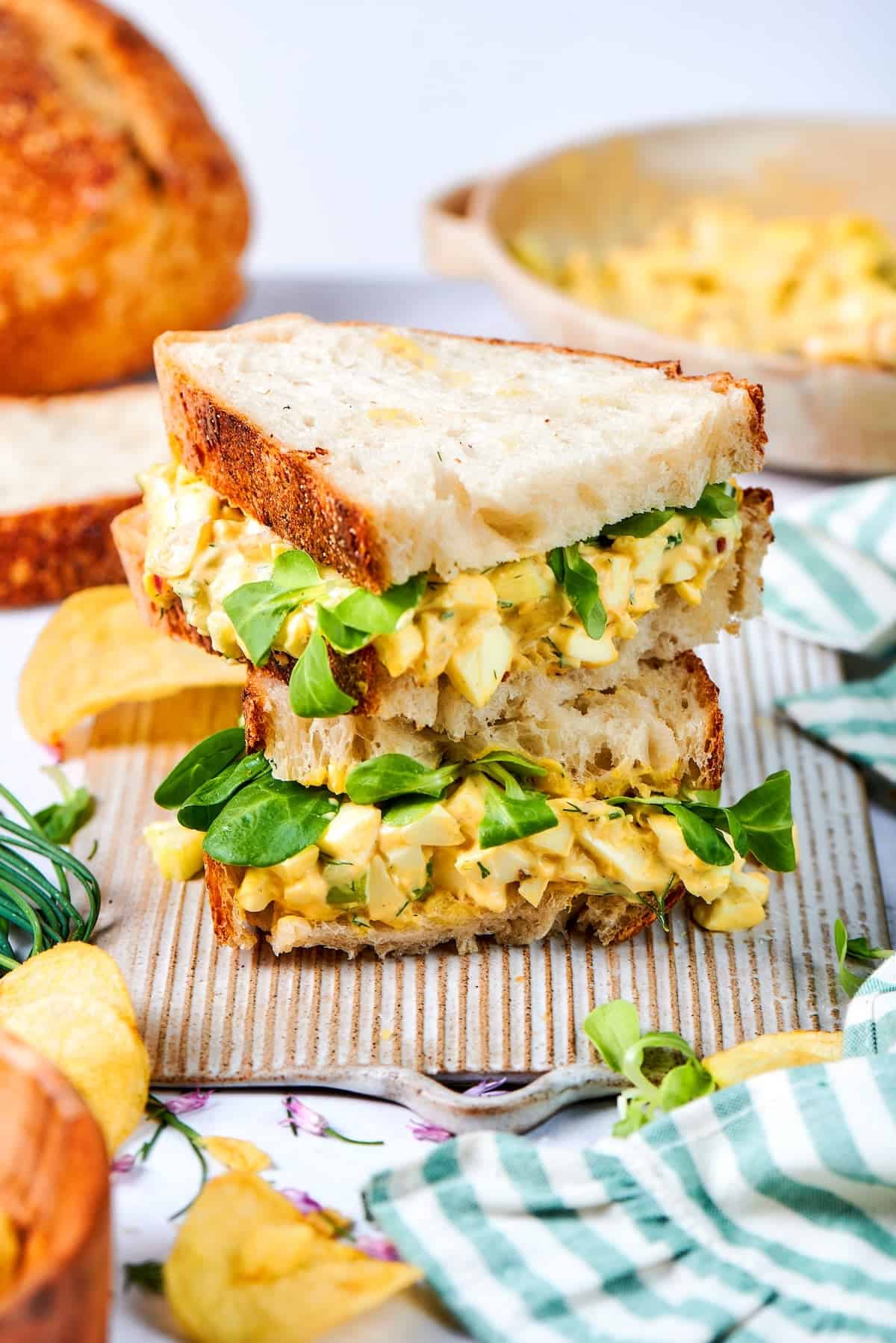 Creamy egg salad gets a fresh lift from bright herbs, making this egg salad sandwich a simple lunch that tastes anything but ordinary! Two egg salad sandwich halves stacked on board.