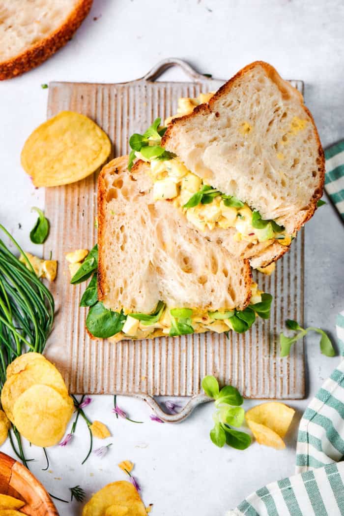 Creamy egg salad gets a fresh lift from bright herbs, making this egg salad sandwich a simple lunch that tastes anything but ordinary! Two egg salad sandwich halves stacked on board.