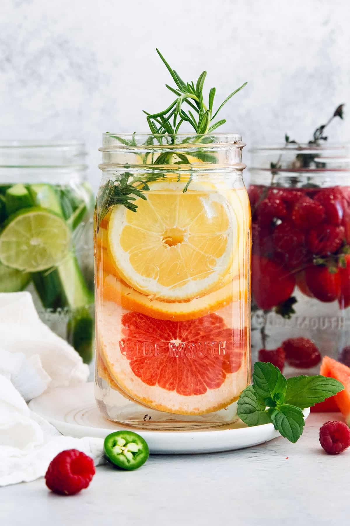Six delicious flavor ideas for making infused spa water at home. Put extra herbs and fruit to use and make staying hydrated so much tastier! Large jar of spa water with lemon, orange, grapefruit, and rosemary