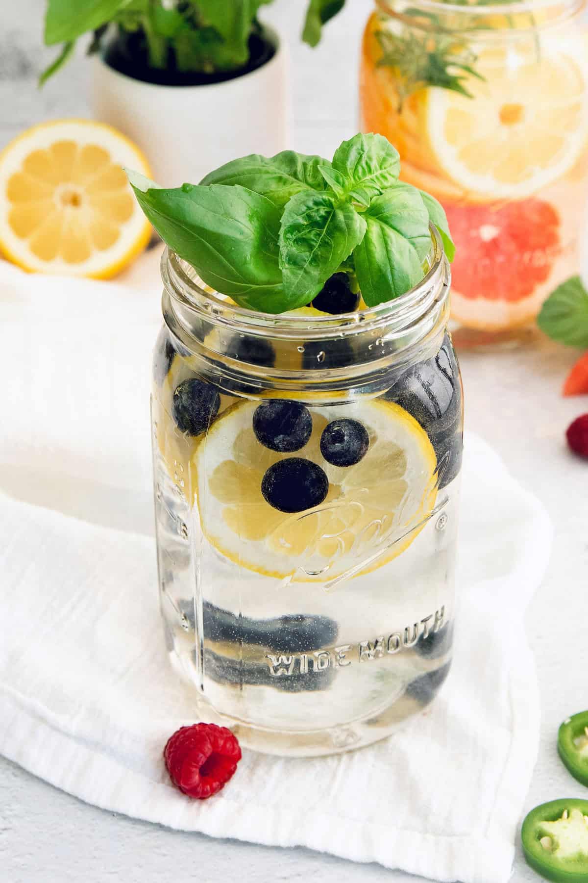 Six delicious flavor ideas for making infused spa water at home. Put extra herbs and fruit to use and make staying hydrated so much tastier! Large jar of spa water with blueberries, basil, and lemon