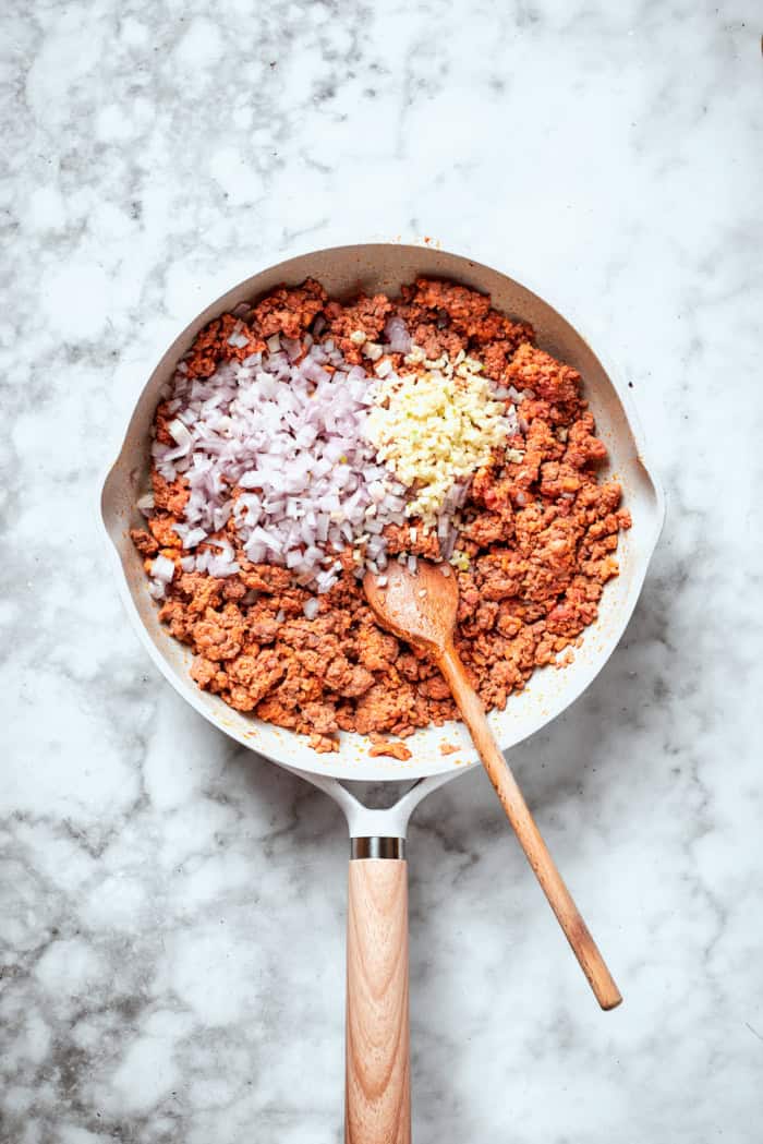 Meaty sauce, super fun spaghetti noodles, and pockets of Cheesy Yum make this Spaghetti Casserole an instant hit with the whole family! Overhead view of onion and garlic added to meat in skillet