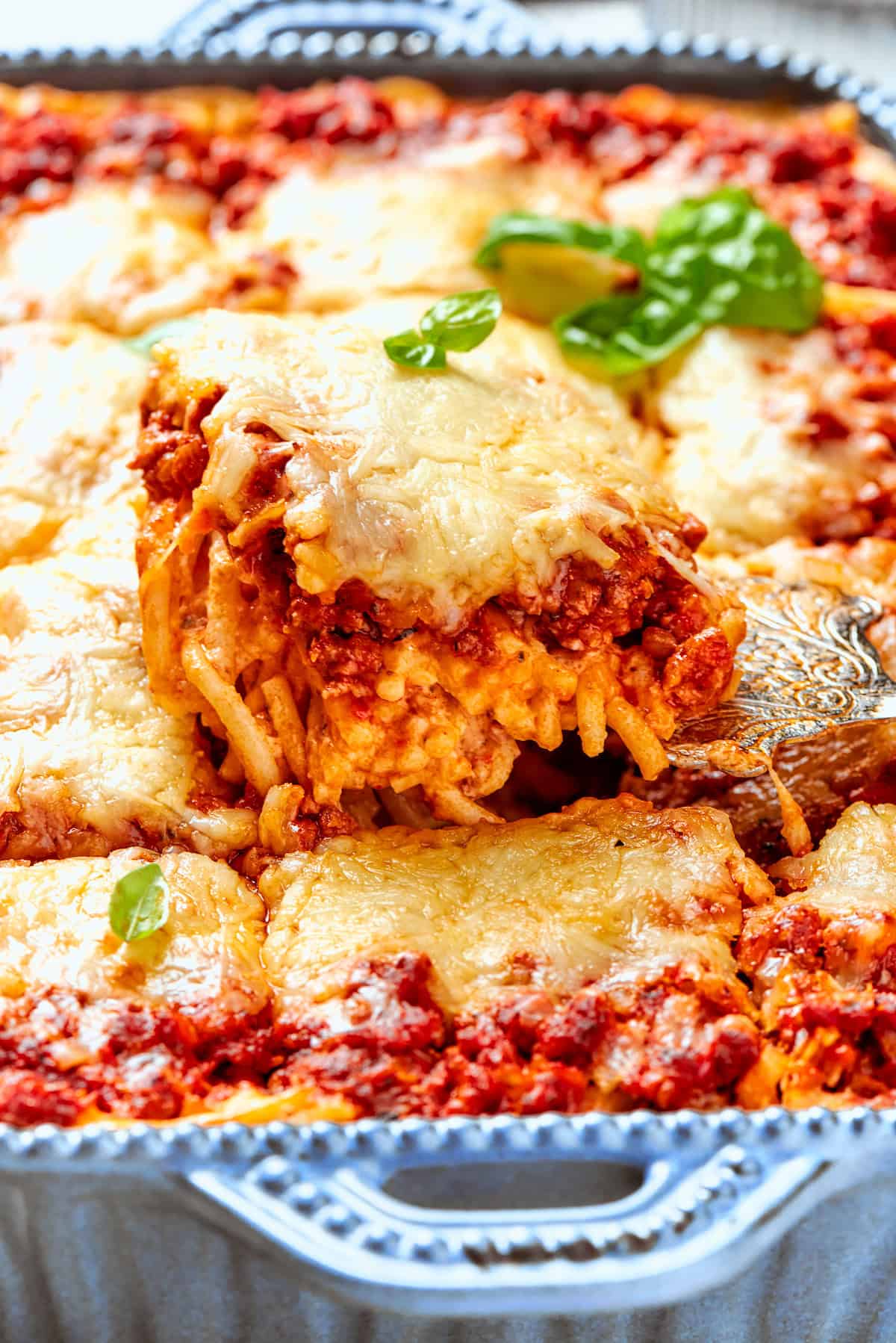 Meaty sauce, super fun spaghetti noodles, and pockets of Cheesy Yum make this Spaghetti Casserole an instant hit with the whole family! Lifting portion of spaghetti casserole from baking dish