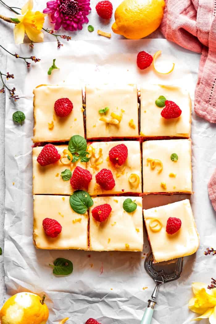 These Lemon Cheesecake Bars with Raspberries are quick to put together, and their lighter texture is perfect for summer. Overhead view of sliced lemon cheesecake bars with raspberries