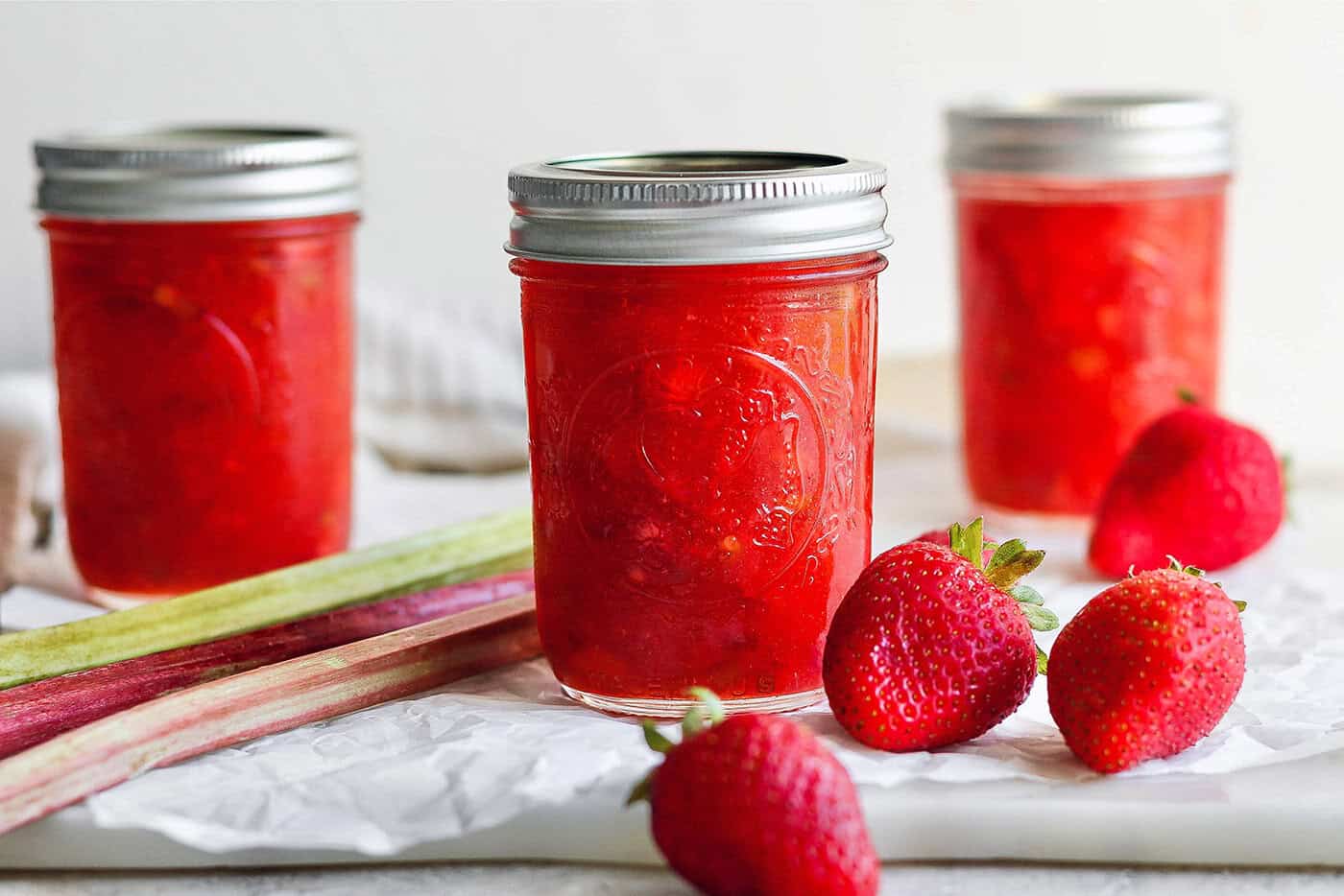 With the right balance of sweet and tart, this strawberry rhubarb freezer jam is a delight — and you don't need canning equipment to make it! Jar of strawberry rhubarb freezer jam with fresh strawberries and rhubarb stalks