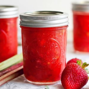 Jar of strawberry rhubarb freezer jam with fresh strawberries and rhubarb stalks