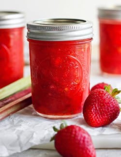 Jar of strawberry rhubarb freezer jam with fresh strawberries and rhubarb stalks