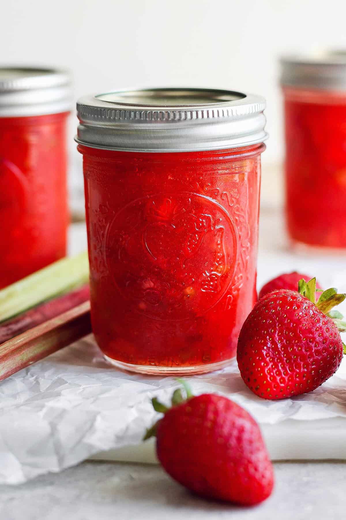 With the right balance of sweet and tart, this strawberry rhubarb freezer jam is a delight — and you don't need canning equipment to make it! Jar of strawberry rhubarb freezer jam with fresh strawberries and rhubarb stalks