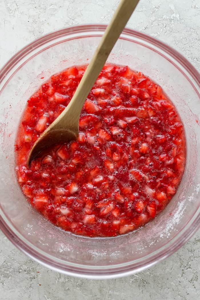 With the right balance of sweet and tart, this strawberry rhubarb freezer jam is a delight — and you don't need canning equipment to make it! Overhead view of strawberries macerated in sugar in bowl with wooden spoon