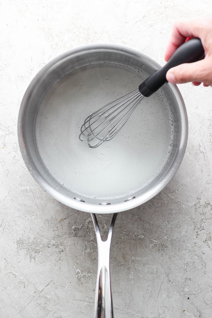 With the right balance of sweet and tart, this strawberry rhubarb freezer jam is a delight — and you don't need canning equipment to make it! Overhead view showing pectin and water being whisked in pan