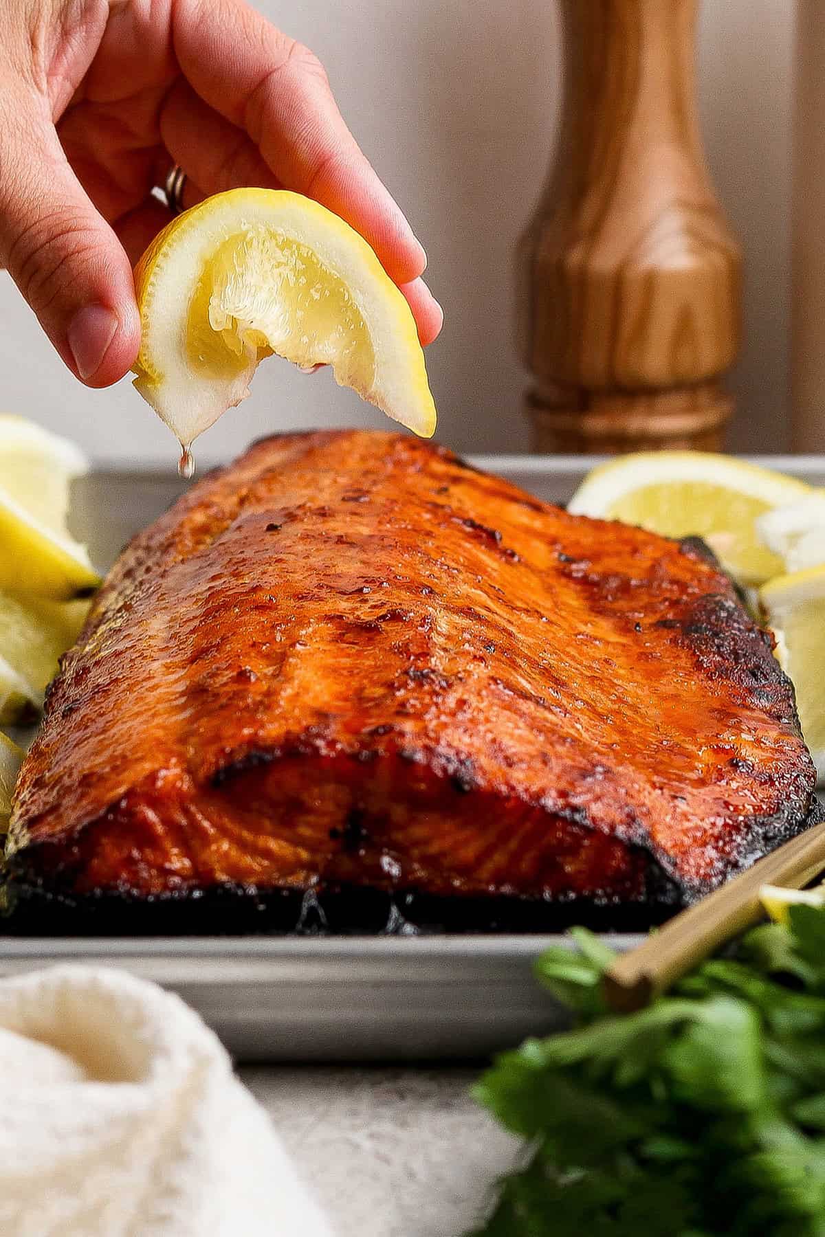 This Sweet and Smoky Grilled Salmon recipe is guaranteed to be perfectly moist, with a smoky maple brown sugar glaze that’s irresistible! Hand squeezing lemon wedge over sweet and smoky grilled salmon