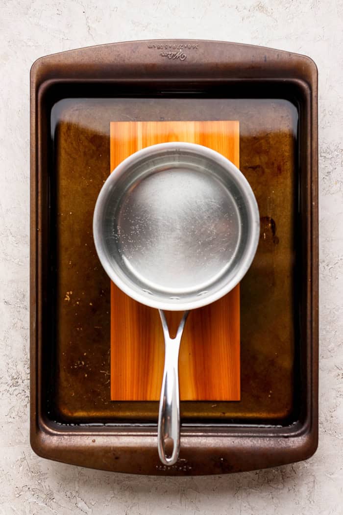 This Sweet and Smoky Grilled Salmon recipe is guaranteed to be perfectly moist, with a smoky maple brown sugar glaze that’s irresistible! Pan set on top of cedar plank in tray of water
