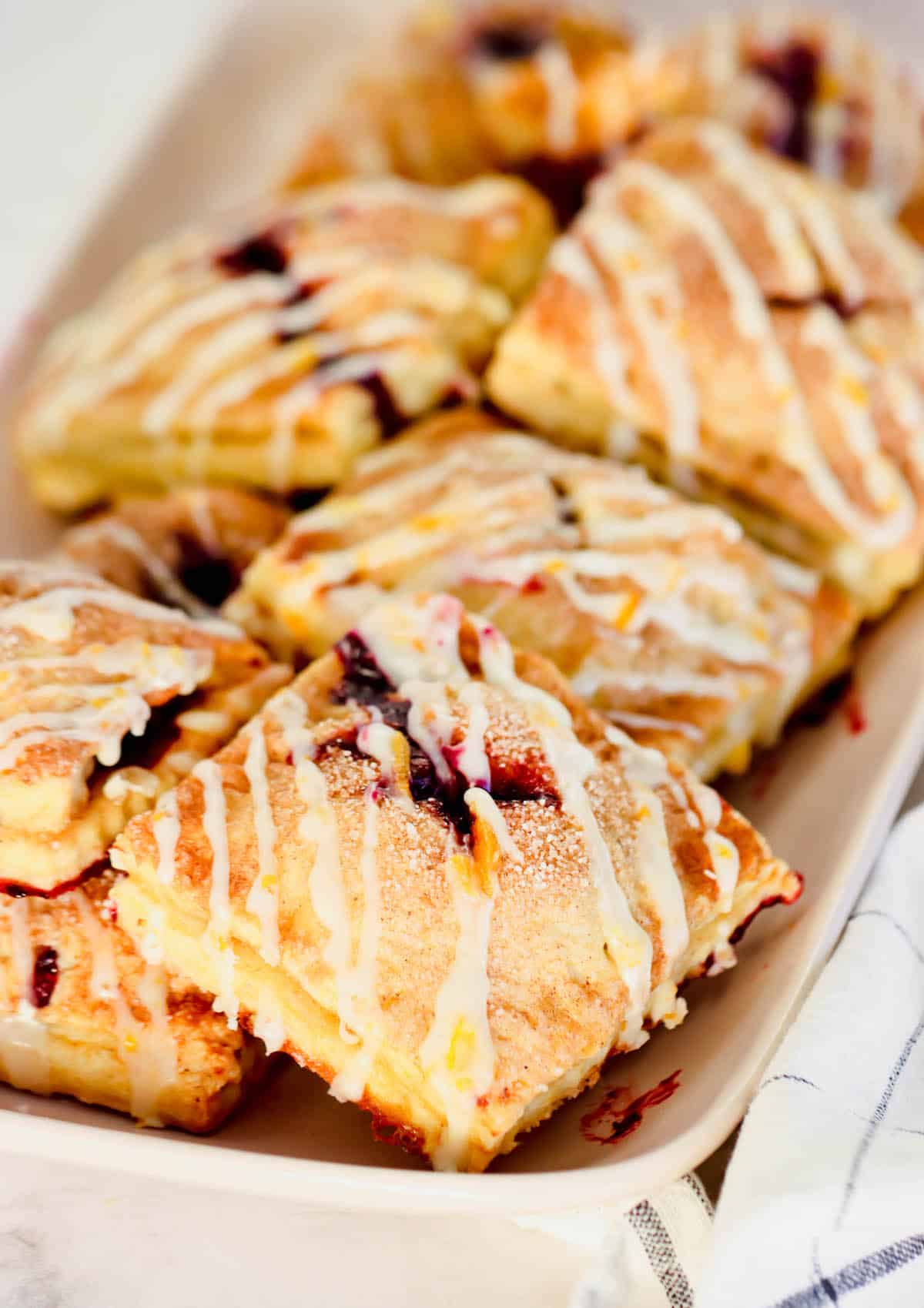 These cute blueberry hand pies combine a flaky pastry crust with sweet blueberry pie filling. It's so much easier than baking a whole pie! Close up of blueberry hand pies drizzled with orange glaze on a long platter.