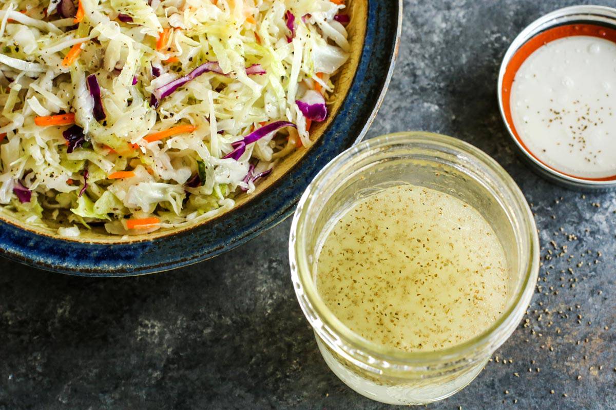 This Sweet Onion Vinegar Coleslaw recipe is fresh, bright & tangy. No mayo here! It has a coleslaw dressing that's seriously good! a jar of vinegar coleslaw dressing and a bowl of coleslaw salad