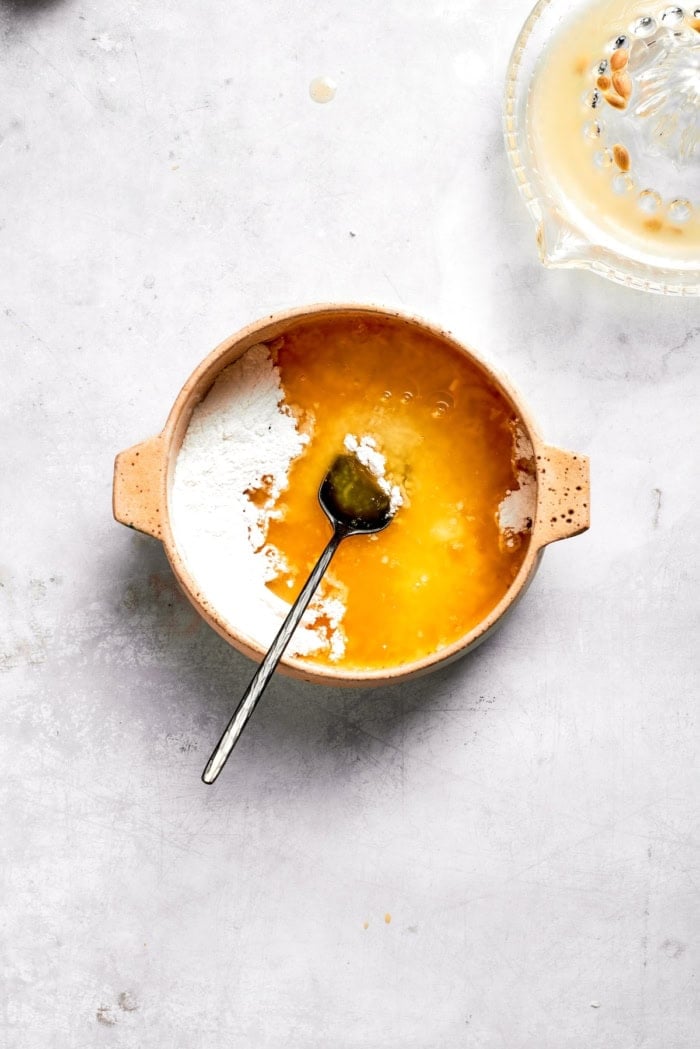 This Almond Lemon Poppy Seed Bread is soft, moist and citrusy. Topped with a zesty glaze, it’s breakfast bread worth getting out of bed for! Ingredients for lemon glaze in bowl with spoon.