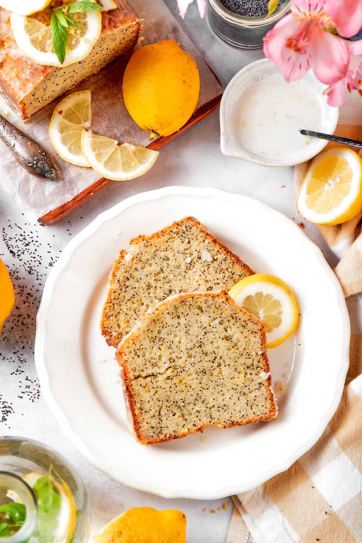 This Almond Lemon Poppy Seed Bread is soft, moist and citrusy. Topped with a zesty glaze, it’s breakfast bread worth getting out of bed for! Two slices of almond lemon poppy seed bread on plate with lemon slice.
