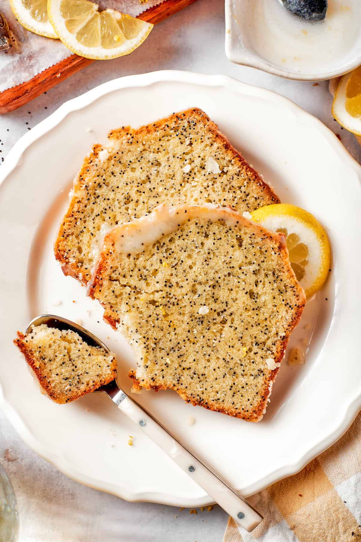 This Almond Lemon Poppy Seed Bread is soft, moist and citrusy. Topped with a zesty glaze, it’s breakfast bread worth getting out of bed for! Spoonful of almond lemon poppy seed bread on plate with two slices.
