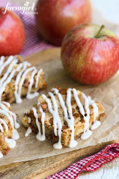 Tender baked apples, sweet cinnamon chips, and a cozy cardamom glaze make these easy homemade apple bars truly special! Whole Wheat Apple Bars on a wood serving board.