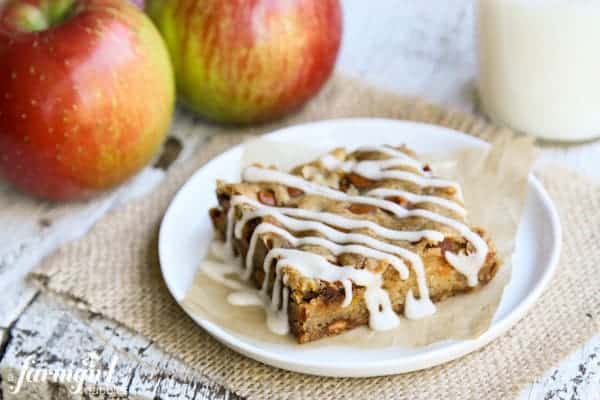Tender baked apples, sweet cinnamon chips, and a cozy cardamom glaze make these easy homemade apple bars truly special! A slice of an Apple Bar with whole, fresh apples.