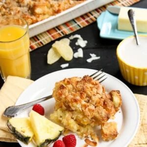 Coconut-Ginger Baked French Toast on a white plate with fresh pineapple and raspberries