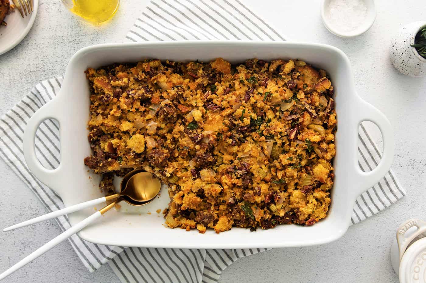 Overhead view of a white casserole dish of cornbread sausage dressing with a serving missing from the corner.