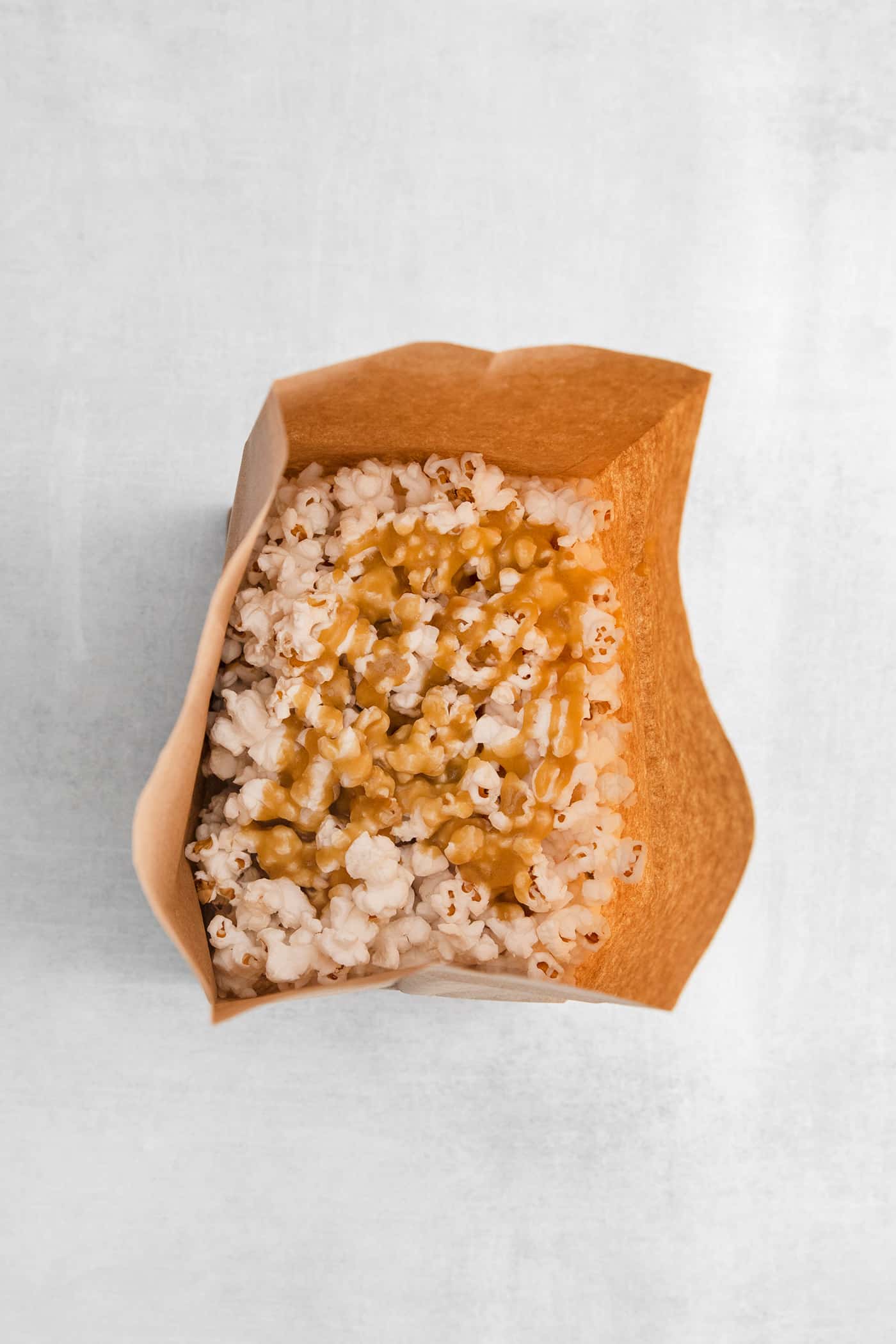 Microwave Caramel Popcorn is ready in just 15 minutes, with a handful of ingredients, a microwave, and a brown paper bag. Caramel drizzled over popcorn in a paper bag