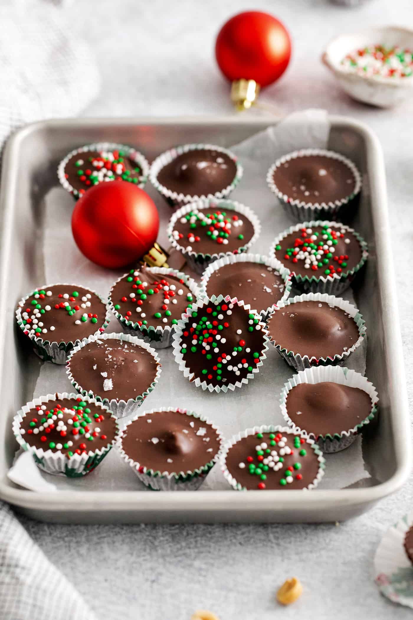 Made with just 5 ingredients, these Homemade Peanut Butter Cups are a million times better than anything you can buy at the store. Peanut butter cups with Christmas sprinkles on a baking sheet