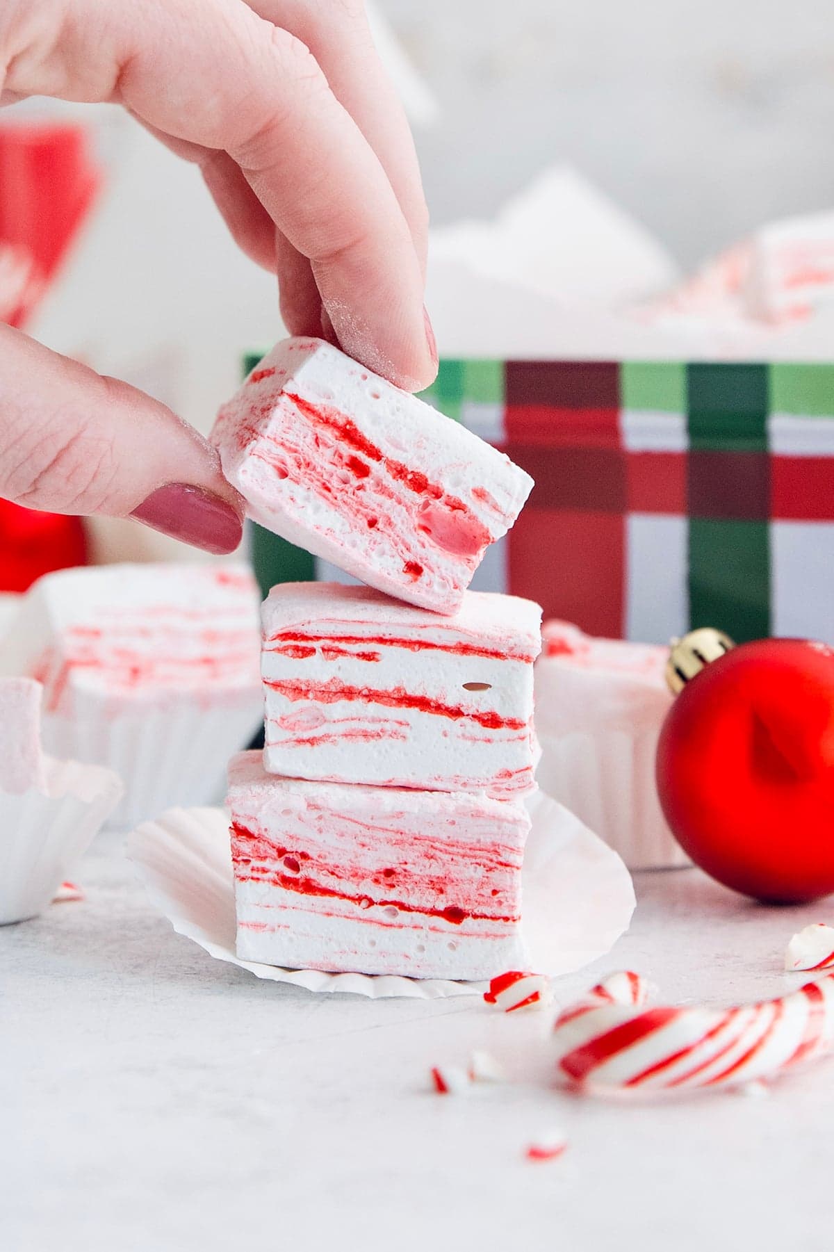 Homemade peppermint marshmallows are fluffy, festive, and so delicious! They're perfect for gifting, hot cocoa, and holiday treats. Hand lifting peppermint marshmallow from stack.