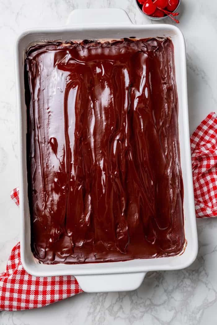 These fudgy cherry brownies are layered with fluffy cherry buttercream and smooth chocolate glaze for an indulgent bakery-style dessert! Chocolate glaze added to pan of cherry brownies.