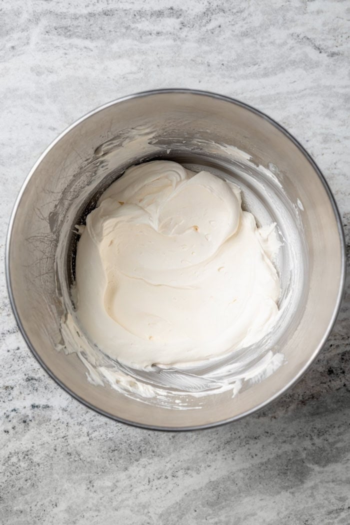 These Angel Food Cupcakes are dotted with mini chocolate chips and topped with vanilla cream and fresh berries. A light, summery treat! Overhead view of whipped vanilla cream frosting in mixing bowl