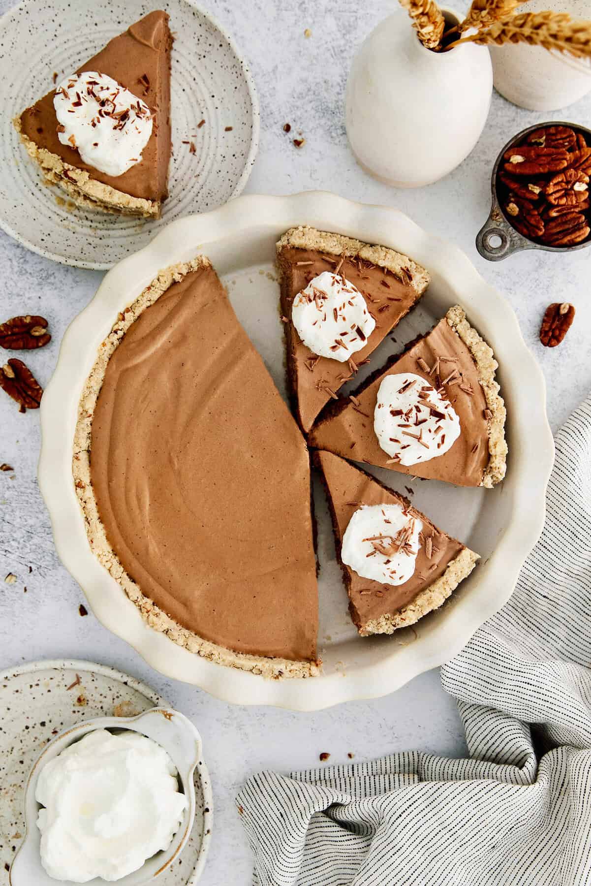 This lighter-than-air French silk pie recipe with 2 types of chocolate, espresso, and a salted pecan crust is a decadent holiday treat. A whole French silk pie with whipped sweetened cream and chocolate shavings on top.