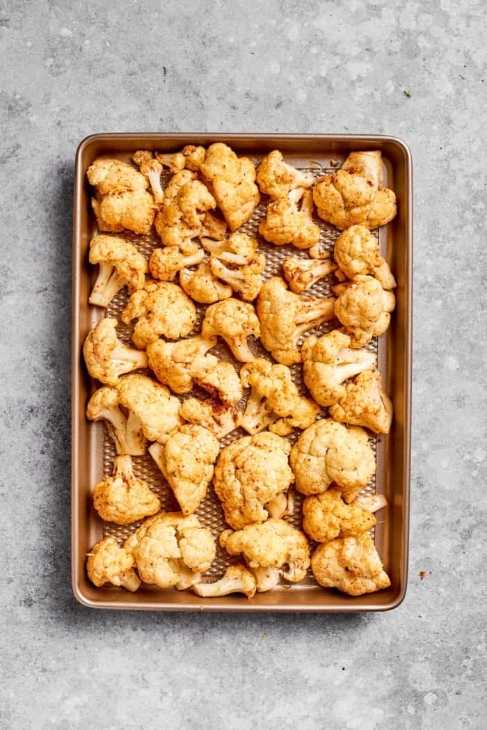 This easy roasted cauliflower is jazzed up with pepitas, cumin, smoky ancho, garlic, and lime. Crispy on the outside, tender inside! Seasoned roasted cauliflower on pan.