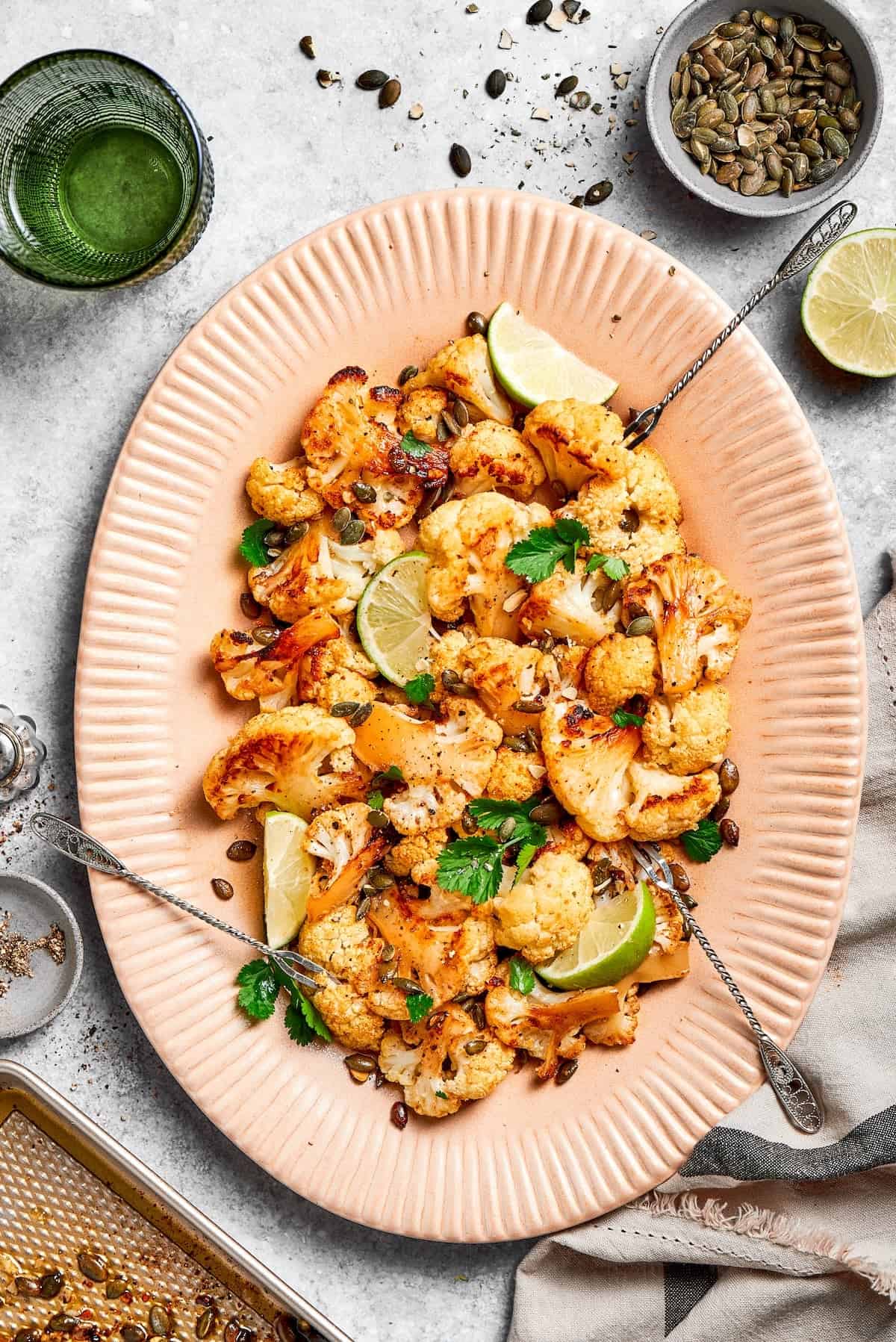 This easy roasted cauliflower is jazzed up with pepitas, cumin, smoky ancho, garlic, and lime. Crispy on the outside, tender inside! Serving plate with Mexican roasted cauliflower and peptias.