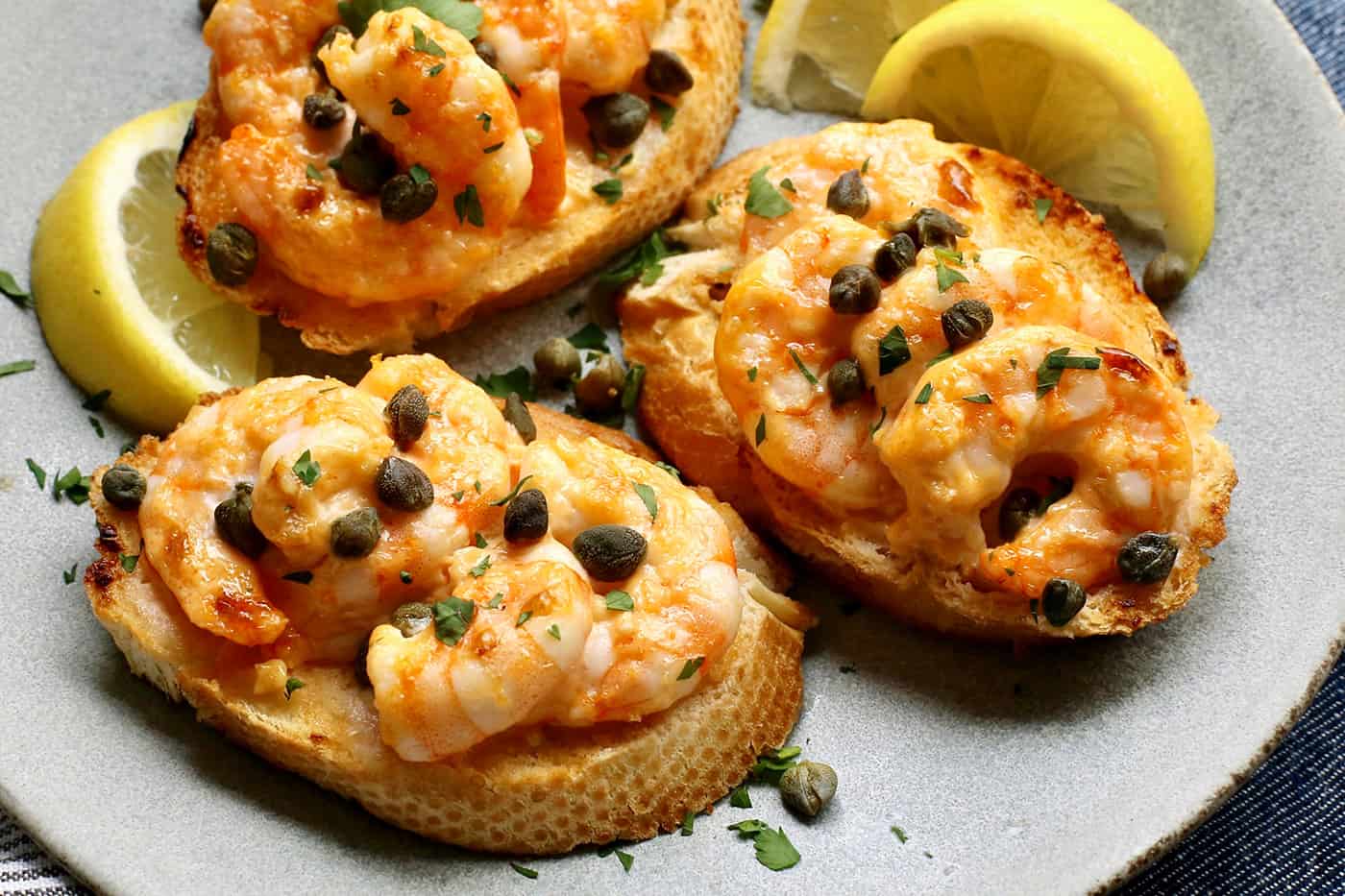Sriracha garlic shrimp toast is made with tender shrimp, spicy sriracha mayo, and lightly crispy toast! An easy appetizer or light meal. Three sriracha shrimp toasts on a gray plate.