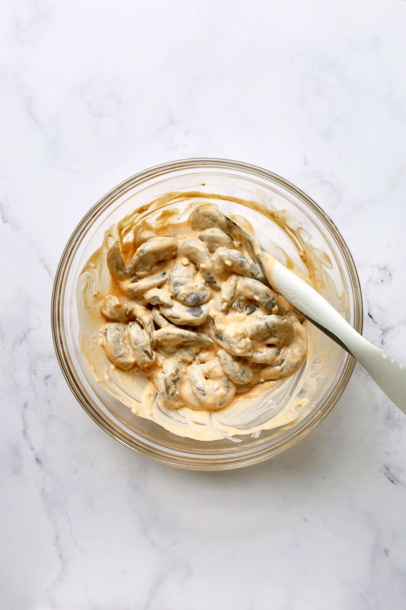 Sriracha garlic shrimp toast is made with tender shrimp, spicy sriracha mayo, and lightly crispy toast! An easy appetizer or light meal. A spoon mixing sriracha mayo with shrimp.