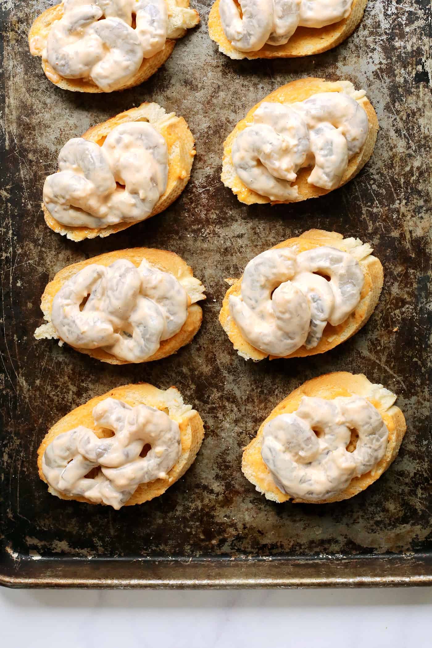 Sriracha garlic shrimp toast is made with tender shrimp, spicy sriracha mayo, and lightly crispy toast! An easy appetizer or light meal. Shrimp toast on a baking sheet.